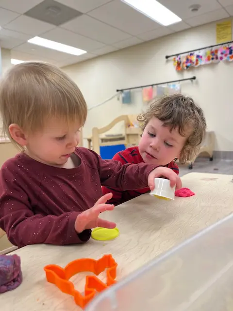 Two toddlers playing with plastic cups and clays